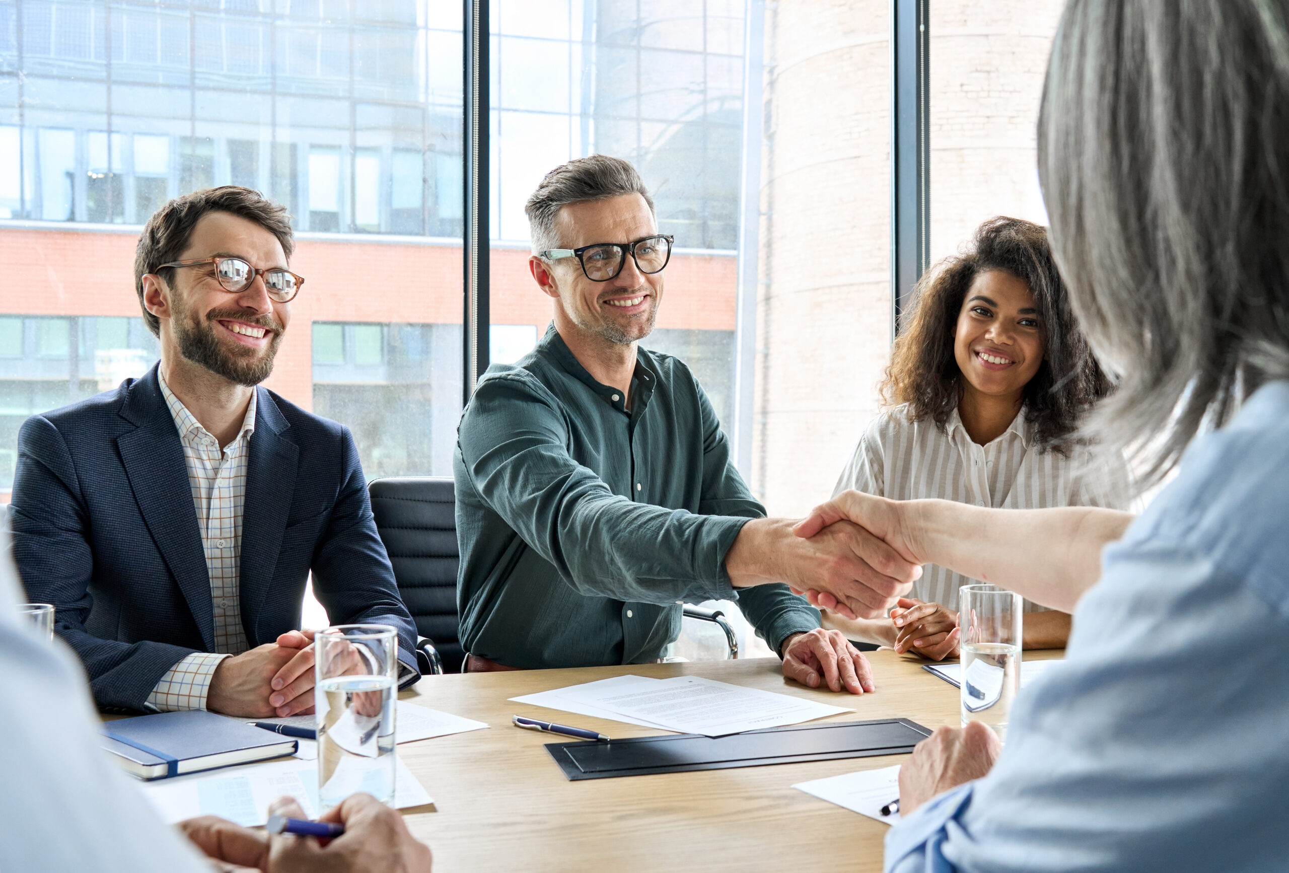 Happy businessman and businesswoman shaking hands at group meeting